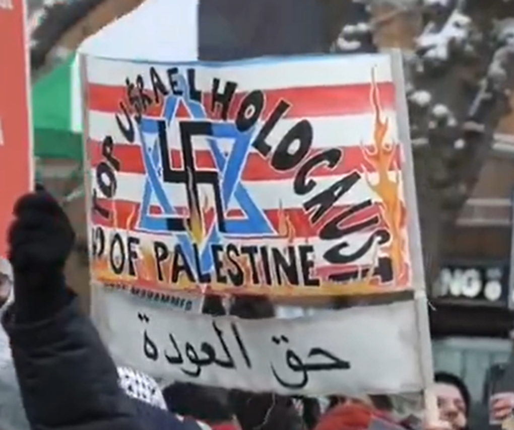 A sign featuring a swastika superimposed over a Star of David on a red-and-white striped background from a January 6, 2025 HCW4P protest