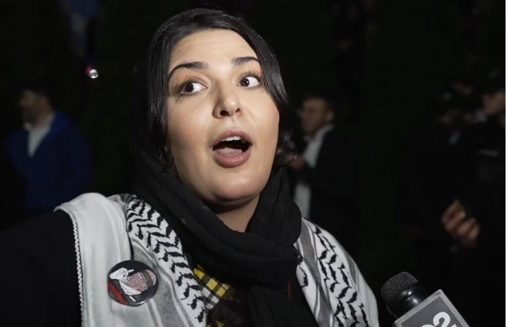 Photo: Anti-Zionist activist and organizer Nerdeen Kiswani wears a pin depicting (now-deceased) Izz ad-Din al-Qassam Brigades spokesperson Abu Obaida at a protest outside Congregation Bnai Yeshurun in Teaneck, NJ on April 1, 2024. (Screenshot/YouTube)