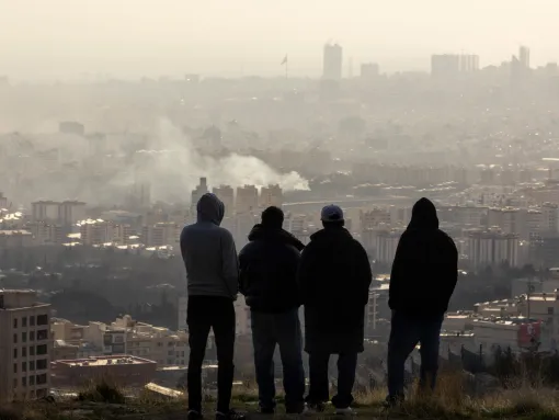 Photo: Men watch from a hillside as a plume of smoke rises after an explosion on March 2, 2026, in Tehran (Majid Saeedi/Getty Images).