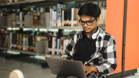 Young positive male student using laptop