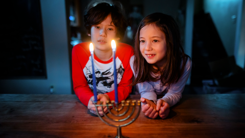 Two children looking at the flames of two candles on a menorah