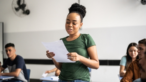 Teen Student standing up and reading a poem out loud to classmates