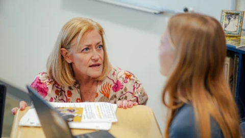 Teacher talking to a student in a classroom by their desk