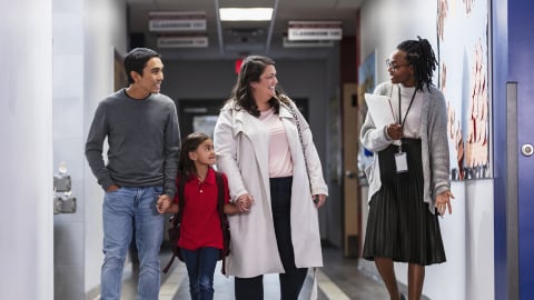 Family walking with their child while talking to teacher in school hallway