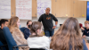 Adult male standing at the front of a classroom of high school students